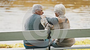 Elderly gray haired couple siting on the bench near the river on autumn day. Romance and old age