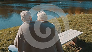 Elderly gray haired couple siting on the bench near the river covering with blanket on autumn day. Romance and old age