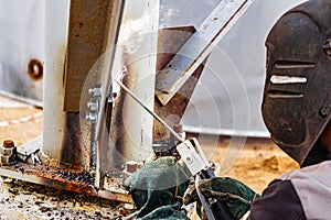 An elderly gray-haired gray-haired welder assembles metal structures at a construction site. Arc welding work. Sparks from welding