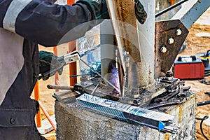 An elderly gray-haired gray-haired welder assembles metal structures at a construction site. Arc welding work. Sparks from welding