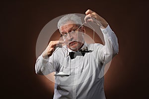 Elderly gray-haired man 50s, in white shirt, glasses and bow tie weighing something on scales with kettlebells