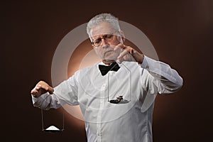 Elderly gray-haired man 50s, in white shirt, glasses and bow tie weighing something on scales with kettlebells