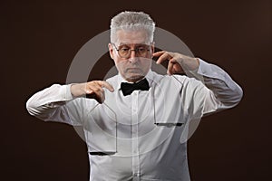 Elderly gray-haired man 50s, in white shirt, glasses and bow tie weighing something on scales with kettlebells