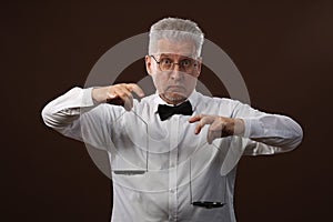 Elderly gray-haired man 50s, in white shirt, glasses and bow tie weighing something on scales with kettlebells