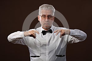 Elderly gray-haired man 50s, in white shirt, glasses and bow tie weighing something on scales with kettlebells