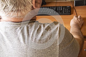 An elderly gray-haired man uses a computer mouse, work at home for the disabled, training pensioners to work on a PC, a view from