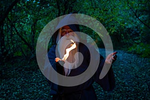 An elderly gray-haired witcher casts a fire spell in the forest. Man in wizard costume