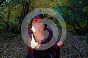 An elderly gray-haired witcher casts a fire spell in the forest. Man in wizard costume