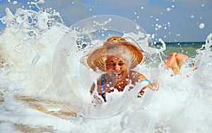 An elderly gray-haired woman lies and laughs and has fun in a straw hat in the waves on the seashore.