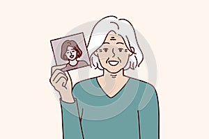 Elderly gray-haired woman shows own old photo for concept of memory of past and nostalgia