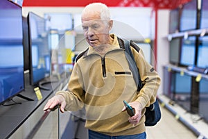 elderly grayhaired man pensioner looking counter with modern digital televisors in showroom of digital goods store