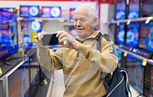 elderly grayhaired man pensioner takes a photos modern digital televisors in showroom of digital goods store