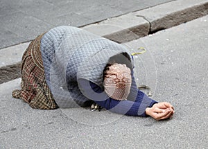 Elderly gypsy woman begging for passersby kneeling with her hand