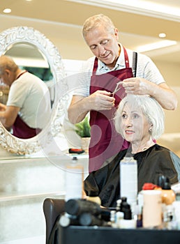 Elderly hairdresser using scissors while providing haircut to woman in salon