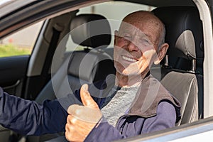 Elderly happy casual man driving the car and shows the thumb