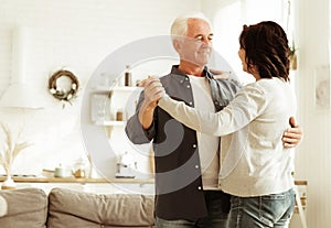 elderly happy couple dancing in the kitchen of their home, love and family concept.