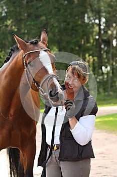 Elderly happy woman and brown horse in the forest