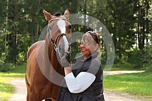 Elderly happy woman and brown horse in the forest