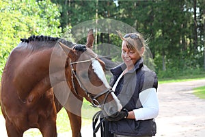 Elderly happy woman and brown horse in the forest