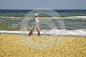 Elderly happy woman running on the beach along the coast near sea