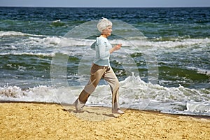 Elderly happy woman running on the beach along the coast near sea