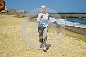 Elderly happy woman running on the beach along the coast near sea