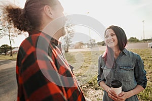 An elderly hipster man with long hair and a beard in a red plaid shirt is talking to a young woman. Summer warm evening