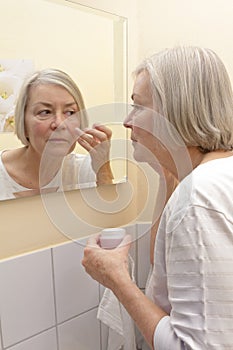 Elderly lady applying cream face