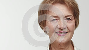 An elderly lady businesswoman with a charming smile opens eyes and raises right eyebrow playfully. Aged woman model