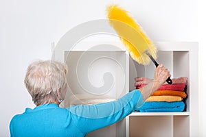 Elderly lady during dusting furniture