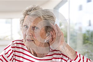 Elderly lady with hearing problems due to ageing holding her hand to her ear as she struggles to hear, profile view on