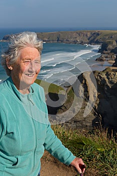 Elderly lady in her eighties with walking stick by beautiful coast scene with wind blowing through her hair
