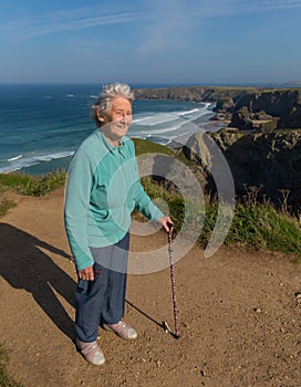 Elderly lady in her eighties with walking stick by beautiful coast scene with wind blowing through her hair