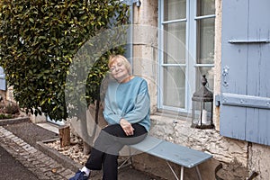 Elderly lady relaxing by her home with greenery and blue shutters