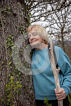 Elderly lady resting against a tree with ivy.