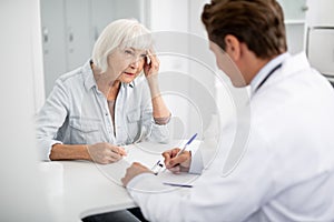 Elderly lady touching her head and looking at the practitioner