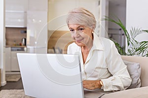 Elderly lady working with laptop. Portrait of beautiful older woman working laptop computer indoors. Senior woman using laptop at