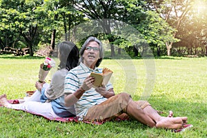 Elderly lifestyle concept. Happiness couple sitting back to back relax together in the public park. Husband reading book