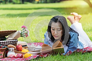 Elderly lifestyle concept. women 50s reading attractive book in her hand have leisure time with picnic have apple, oranges
