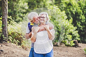 Elderly lifestyle people with couple of caucasian active senior kissing in relationship with green plants nature in background -