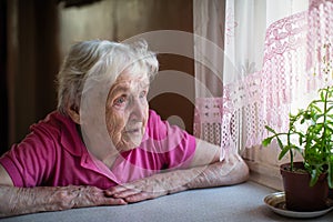 Elderly lone woman looks sadly out the window