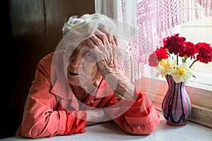 Elderly lone woman looks sadly sitting near the window.