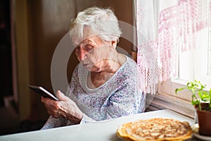 Elderly lone woman sits with a smartphone in her hands.
