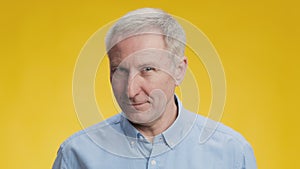Elderly lovelace. Playful mature senior grey-haired man playing with his eyebrow, flirting to camera, yellow background