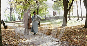 Elderly, lovely married couple with bouquet of flowers walking in autumn park