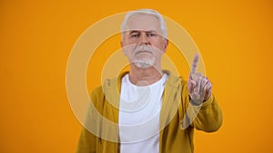 Elderly male in casual clothes showing warning finger gesture, rejection sign