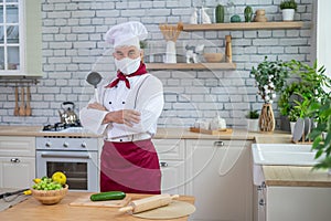 An elderly male chef wearing a mask in the kitchen crossed his arms over chest