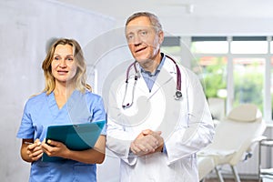 Elderly male doctor with female assistant standing in medical office