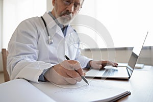 Elderly male doctor fill patient anamnesis in medical journal