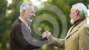 Elderly male friends shaking hands, happy to see each other, brothers meeting